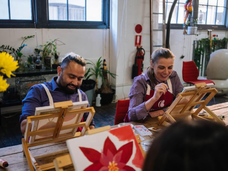a man and a woman smiling while painting on portable easels